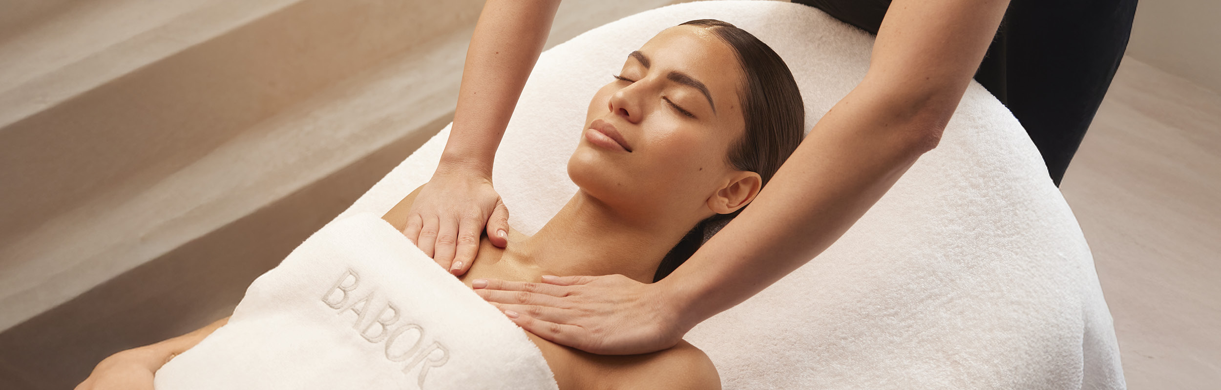 Frau mit geschlossenen Augen auf einer Liege, zwei Hände massieren