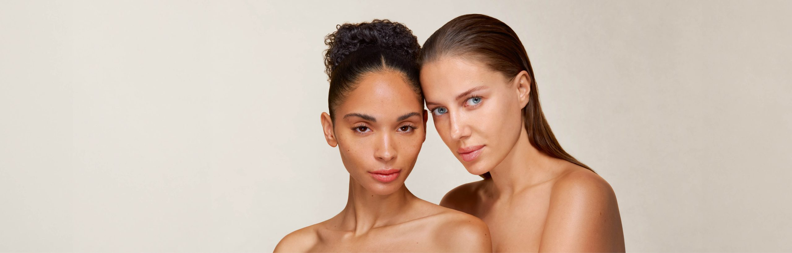 Zwei Frauen mit strahlender Haut, Schulter an Schulter und Blick in die Kamera.