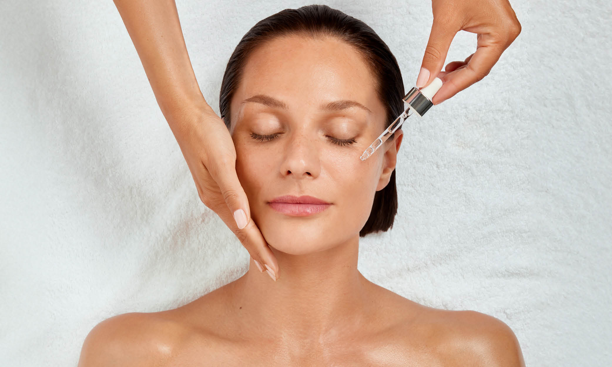 Frau mit geschlossenen Augen, Hand stützt die Wange, Pipette träufelt Serum aufs Gesicht